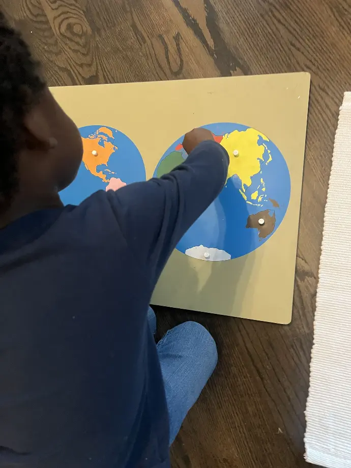 A young Black child is putting a pin on a world map.