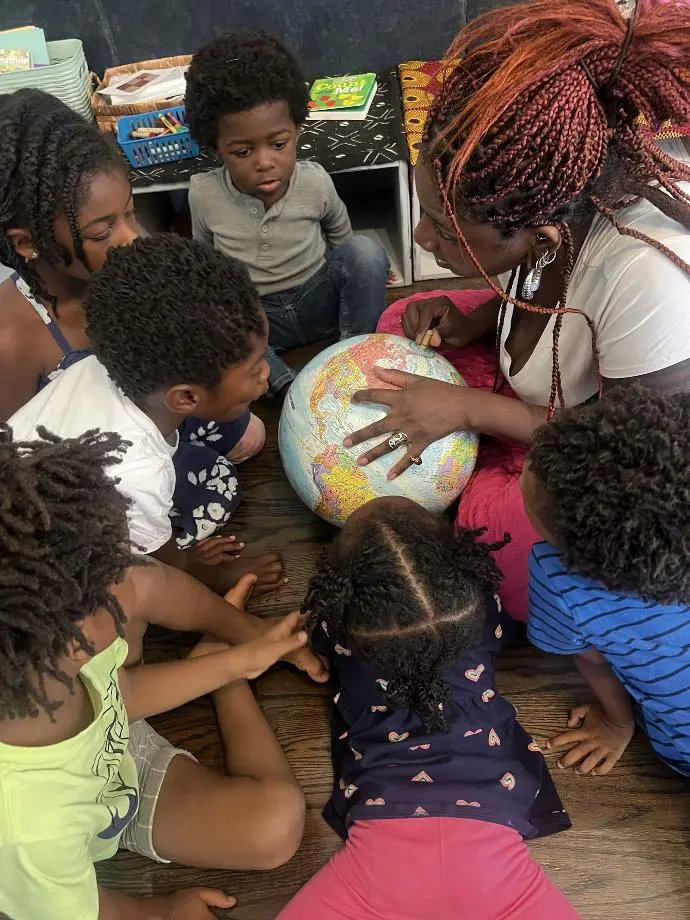 A teacher is pointing to a globe and talking to her students.