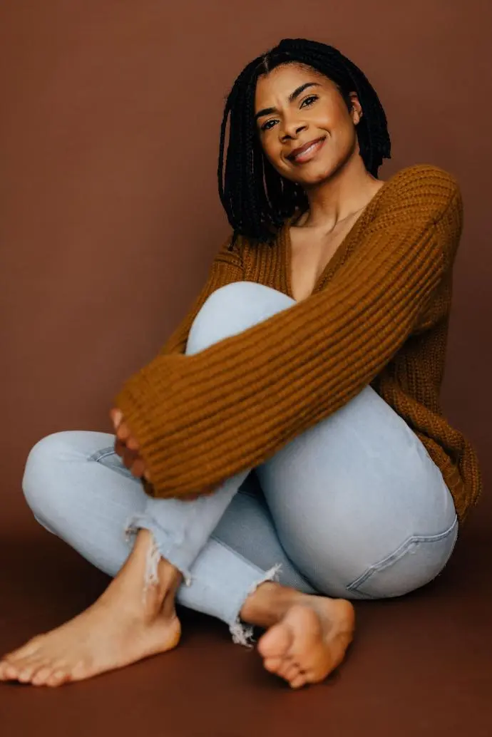 A woman sitting on the ground in front of a brown backdrop