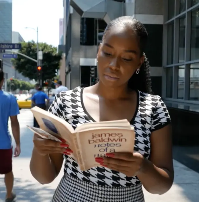 Black woman walking through the street reading book.