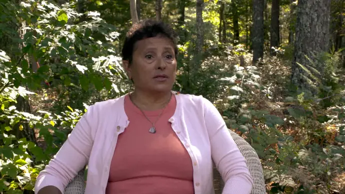 A Wampanoag woman sits in a chair outside.