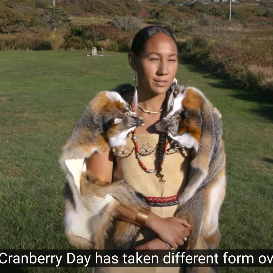 A Wampanoag woman stands outside in the traditional clothes of her people.