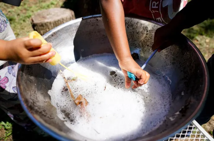 Hands of young children swirling objects into a soapy bowl.