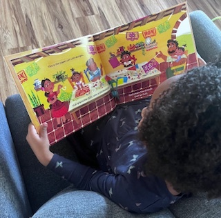 Young Black girl sitting and reading a colorful book.