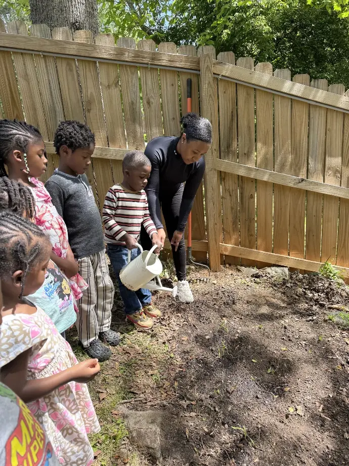 A teacher and children watering soil.